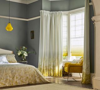 Yellow and gray bedroom with patterned curtains, yellow chair and woven rug