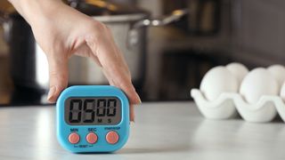 Woman holding the top of a blue kitchen timer on a countertop