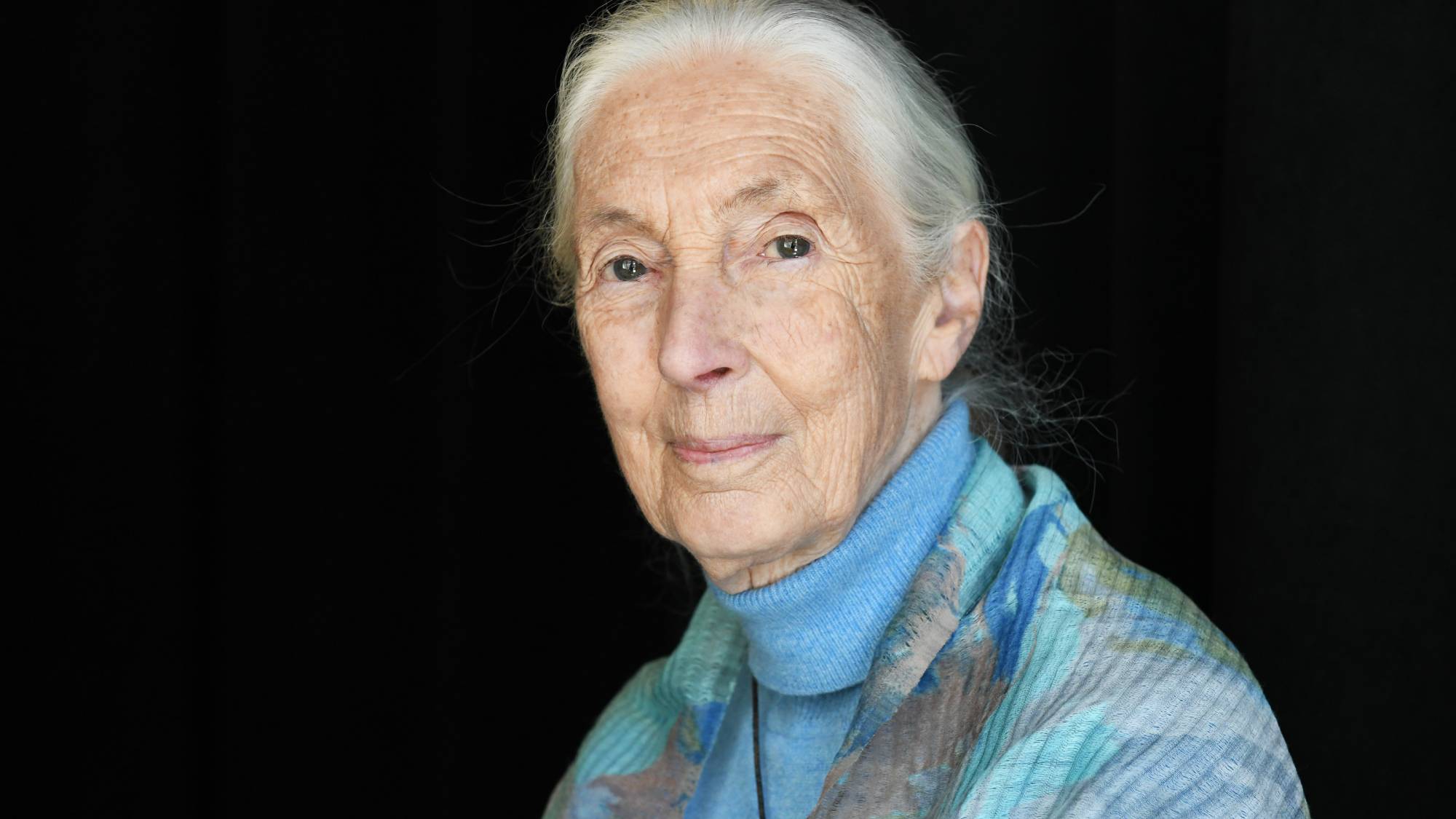 Jane Goodall smiles into the camera in front of a black background