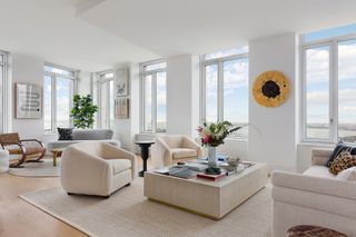 large open plan living room with two seating areas. one in the corner with woven chair and plant, the other in the middle of the room with two beige armchairs, a large stone coffee table decorated with books and flowers, and a white sofa opposite