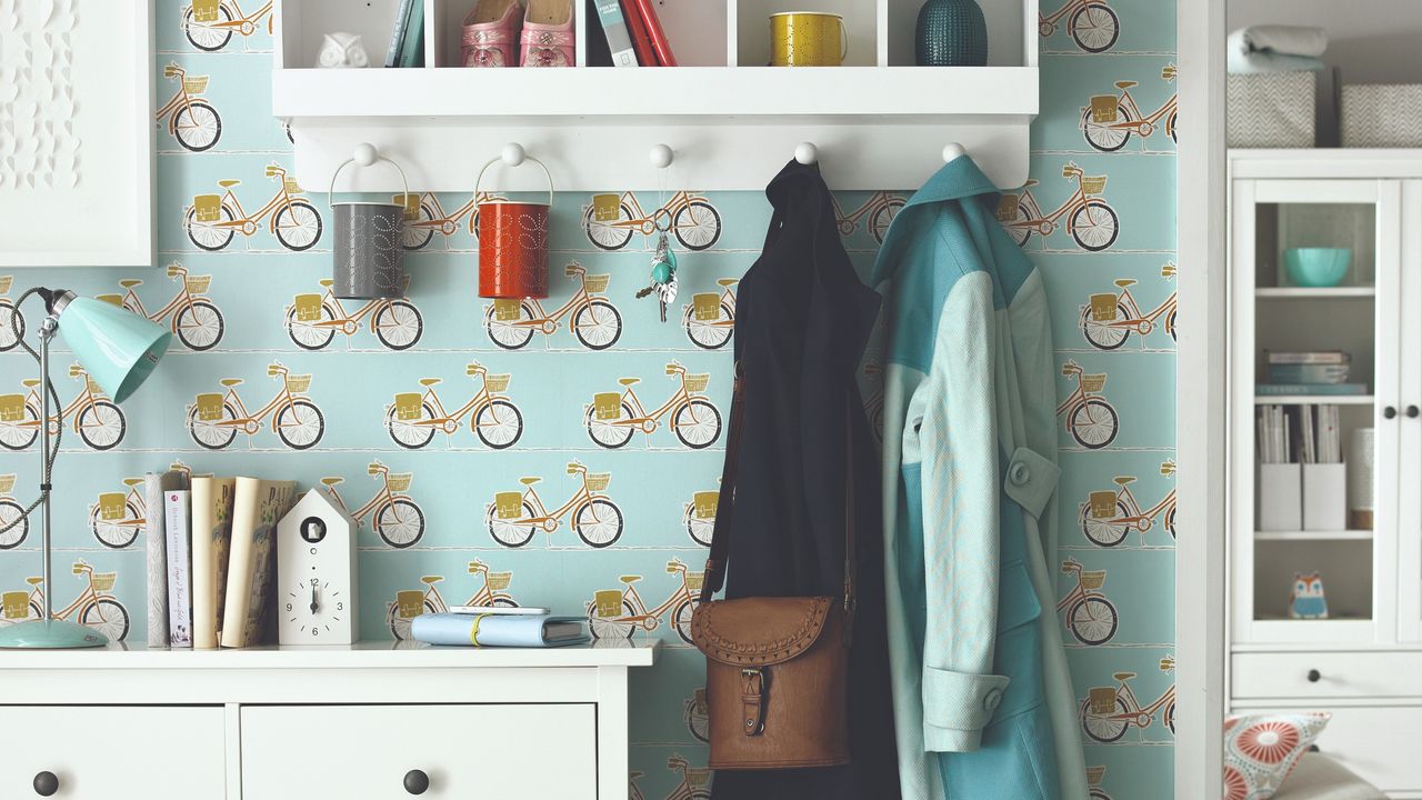 A hallway covered in a bicycle-print wallpaper with a shelf peg rail on the wall and an IKEA shoe cabinet