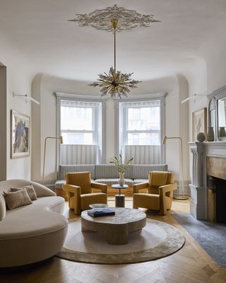 A living room with a curving sofa in beige, two yellow armchairs and a low, round coffee table