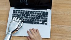 A human right hand and a robot left hand using a MacBook.