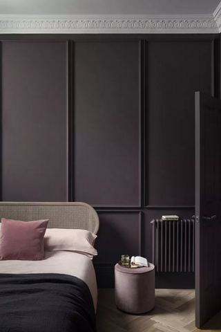A deep aubergine bedroom with panelled walls, a rattan bed and pale pink accessories