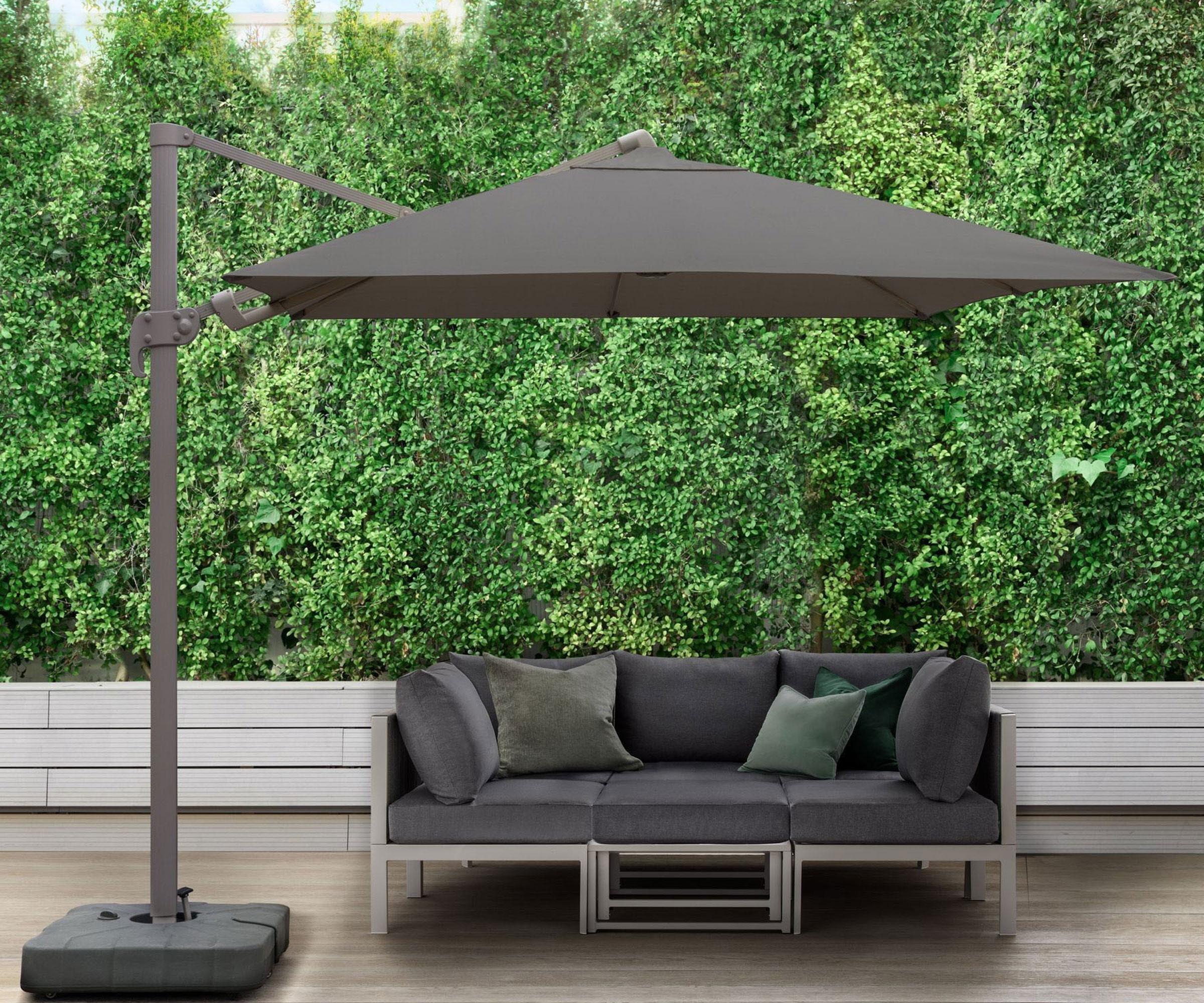 large dark grey cantilevered parasol shading a dark grey garden sofa with cushions on a garden deck area