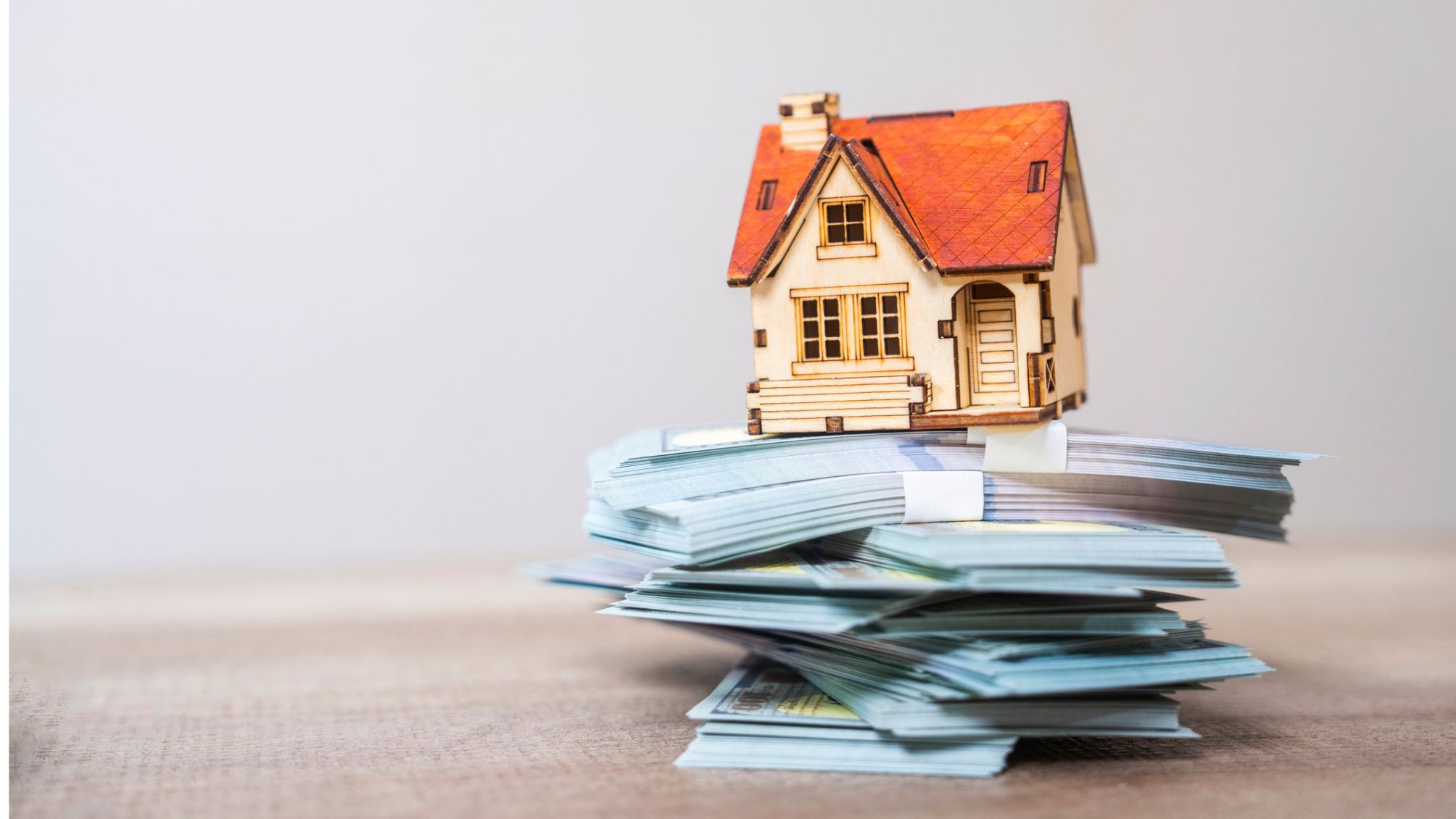 A model home sitting on top of a pile of cash.
