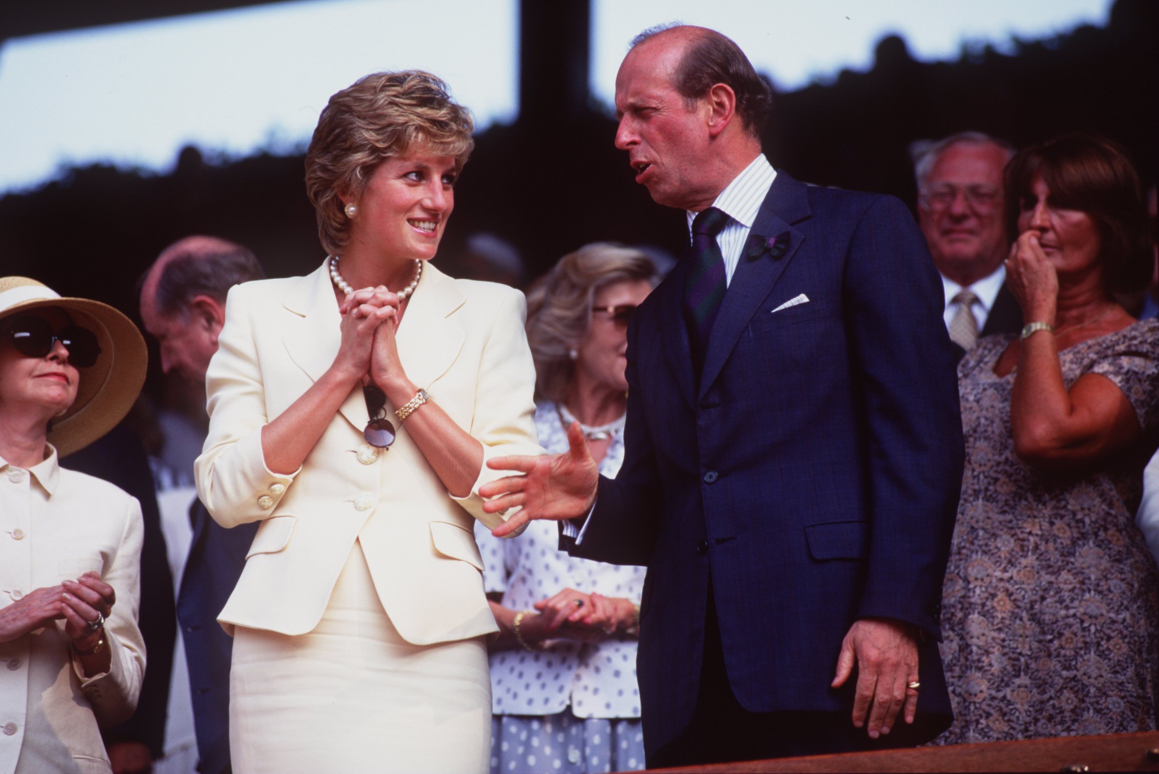 Princess Diana wearing a pale yellow skirt suit talking to the Duke of Kent at Wimbledon