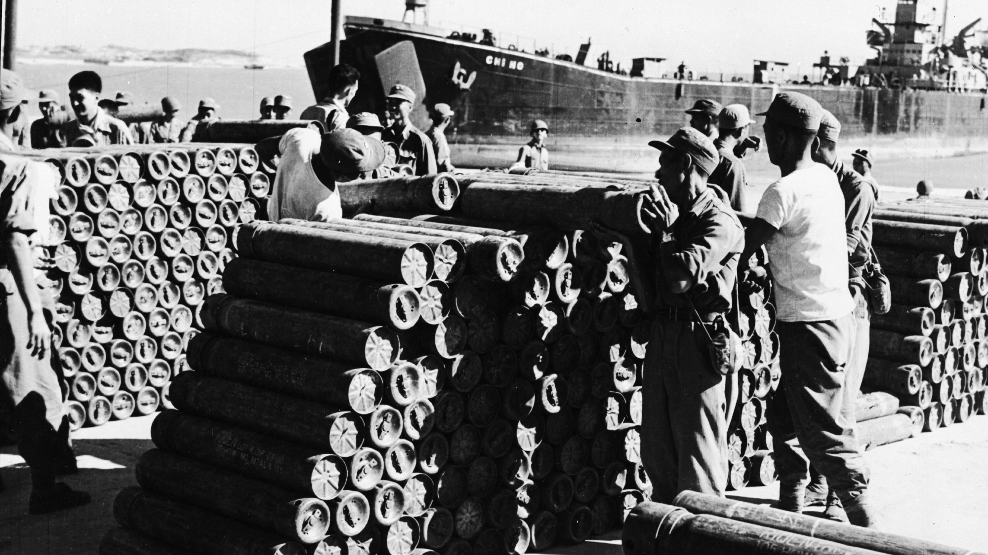 black and white photograph depicting military personnel stacking armaments at a coastal location