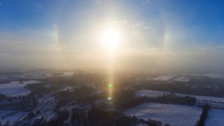 a bright sun rises above a snowy landscape