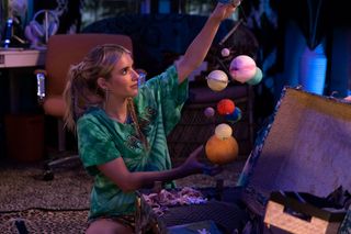a sitting woman in a green t shirt holds a small model of the solar system