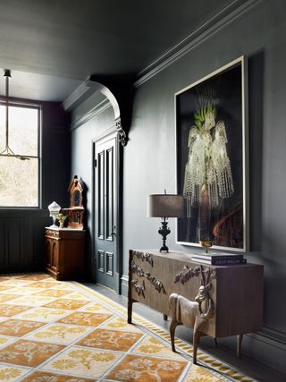 hallway with dark gray walls and carved wooden sideboard and bright rug