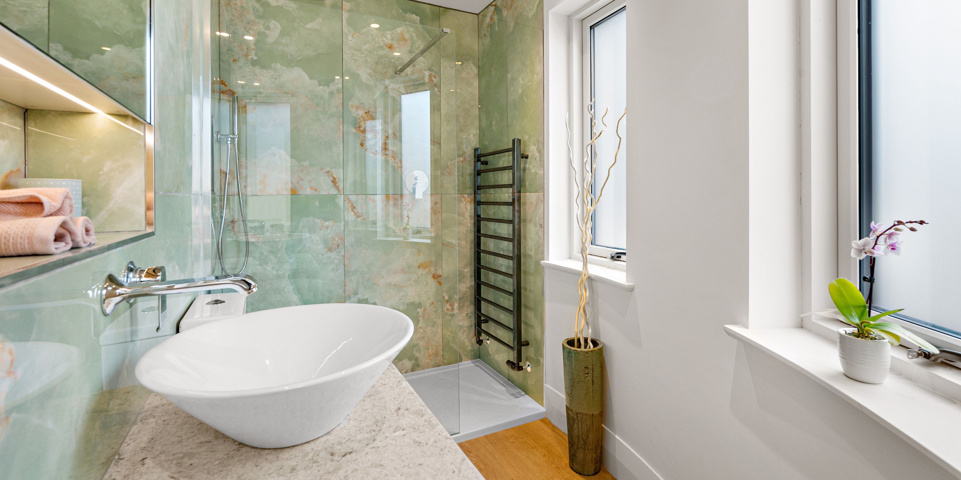 A bathroom with white walls and green onyx tiles in the shower