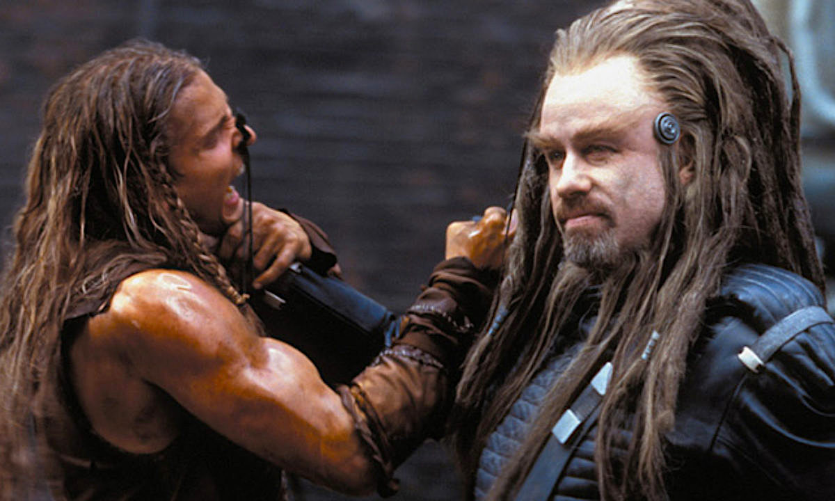 A weird alien with dreadlocks lifts a smaller human tribesman