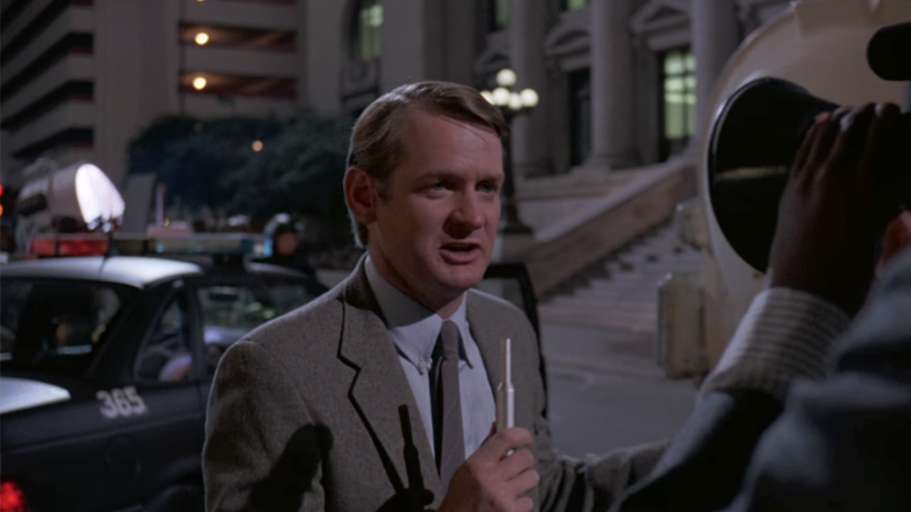 Bill Farmer as a reporter, in front of a camera in RoboCop