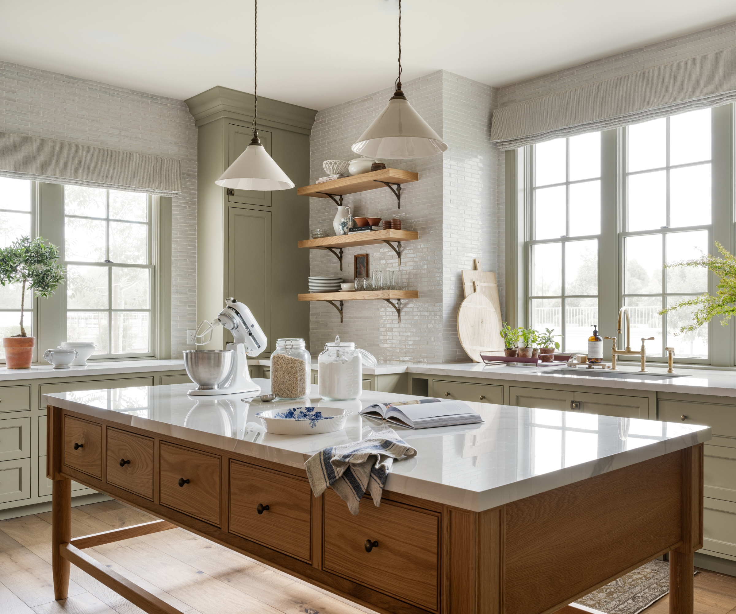 A timeless kitchen with pale green cabinets, a wood freestanding island, open shelving, and white tile walls