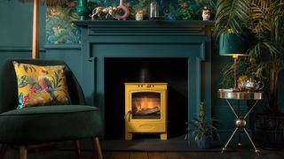 yellow log burning stove in teal painted fireplace in green living room with botanical wallpaper