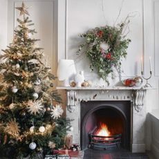 A fireplace decorated with Christmas baubles and a wreath hung above it, alongside a decorated Christmas tree next to it