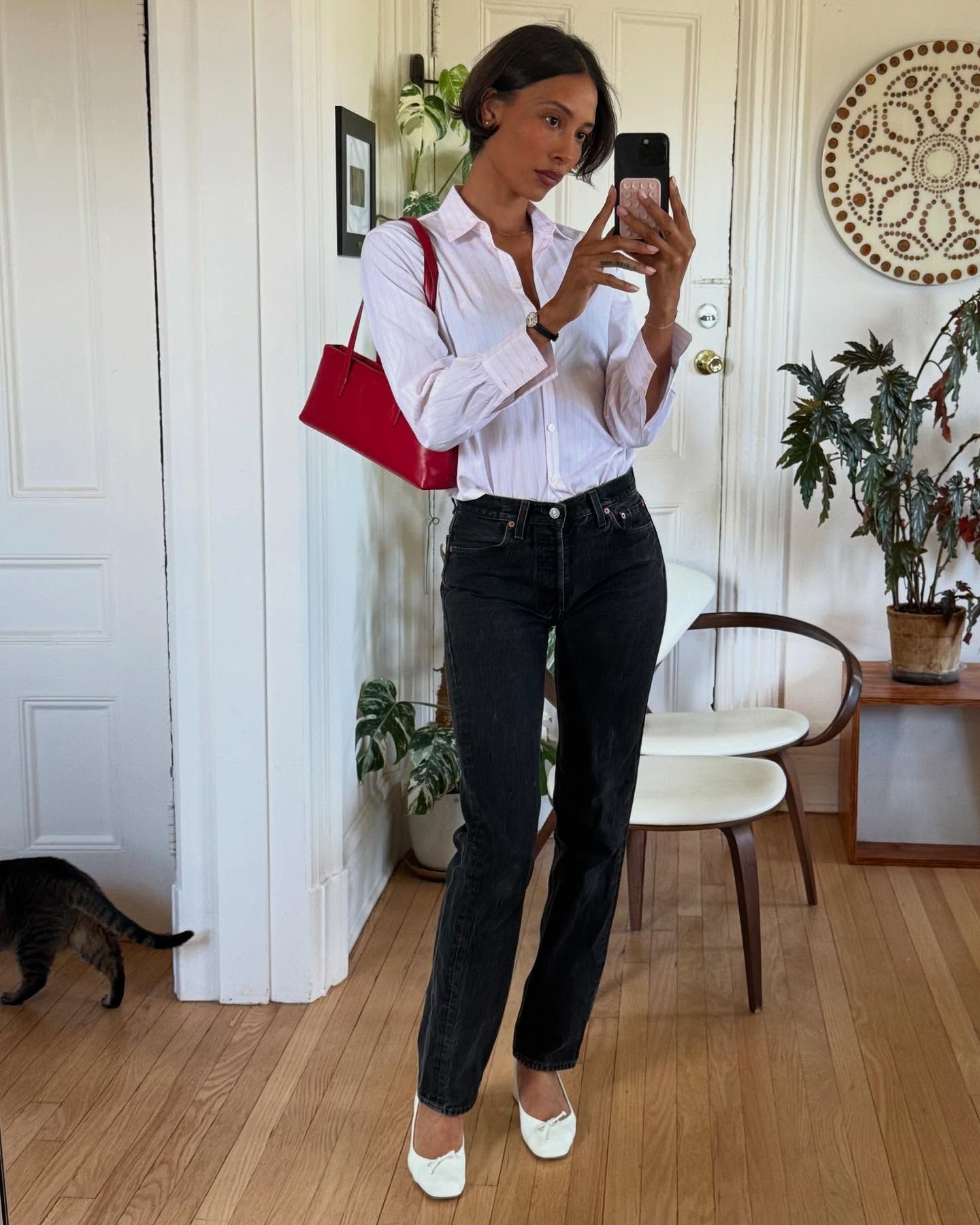 Tylynn wears a white blouse, black jeans, white flats, and a red bag.