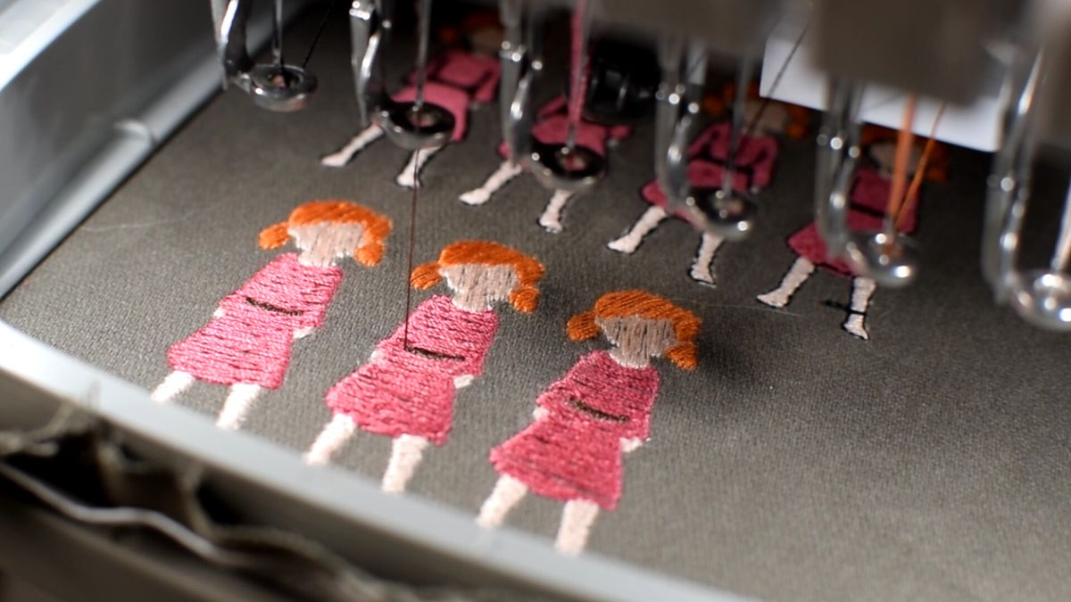 Close up of sprites of young girl in pink dress being embroidered on dark cloth