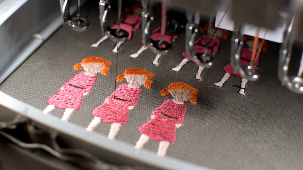 Close up of sprites of young girl in pink dress being embroidered on dark cloth