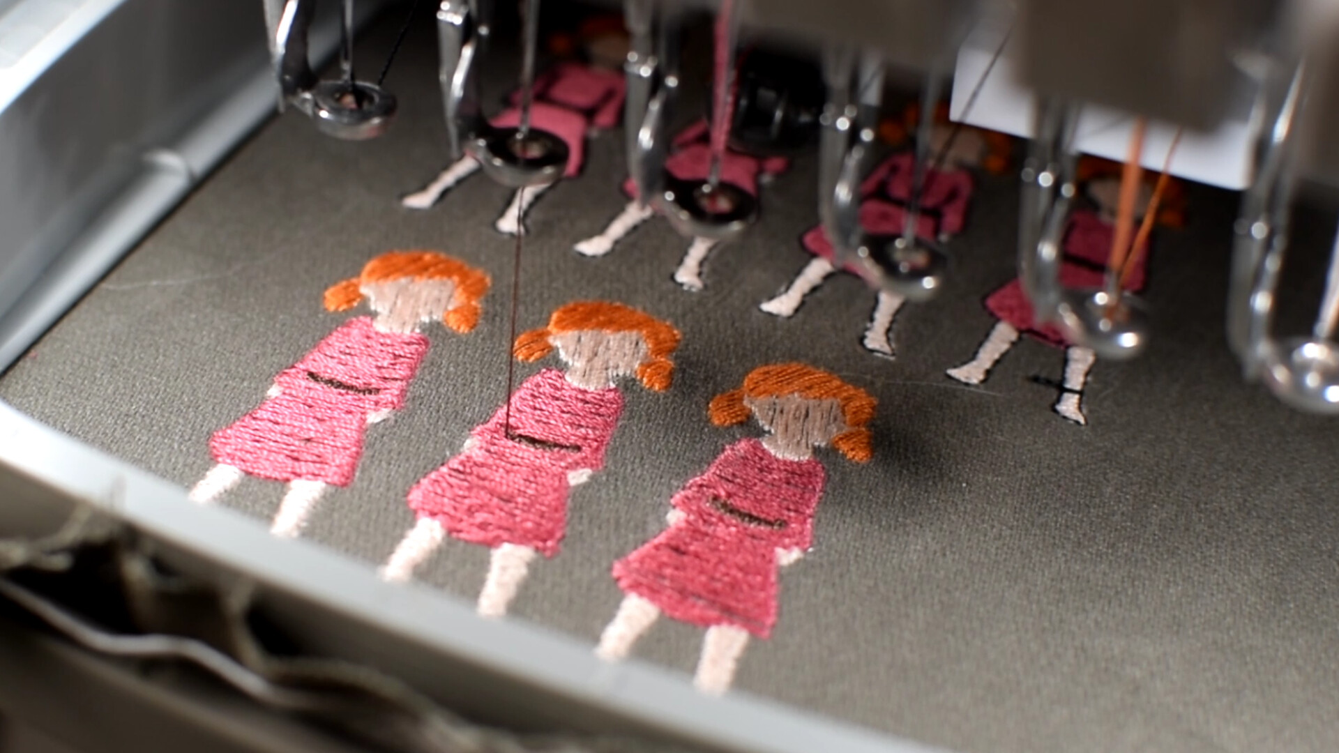 Close up of sprites of young girl in pink dress being embroidered on dark cloth
