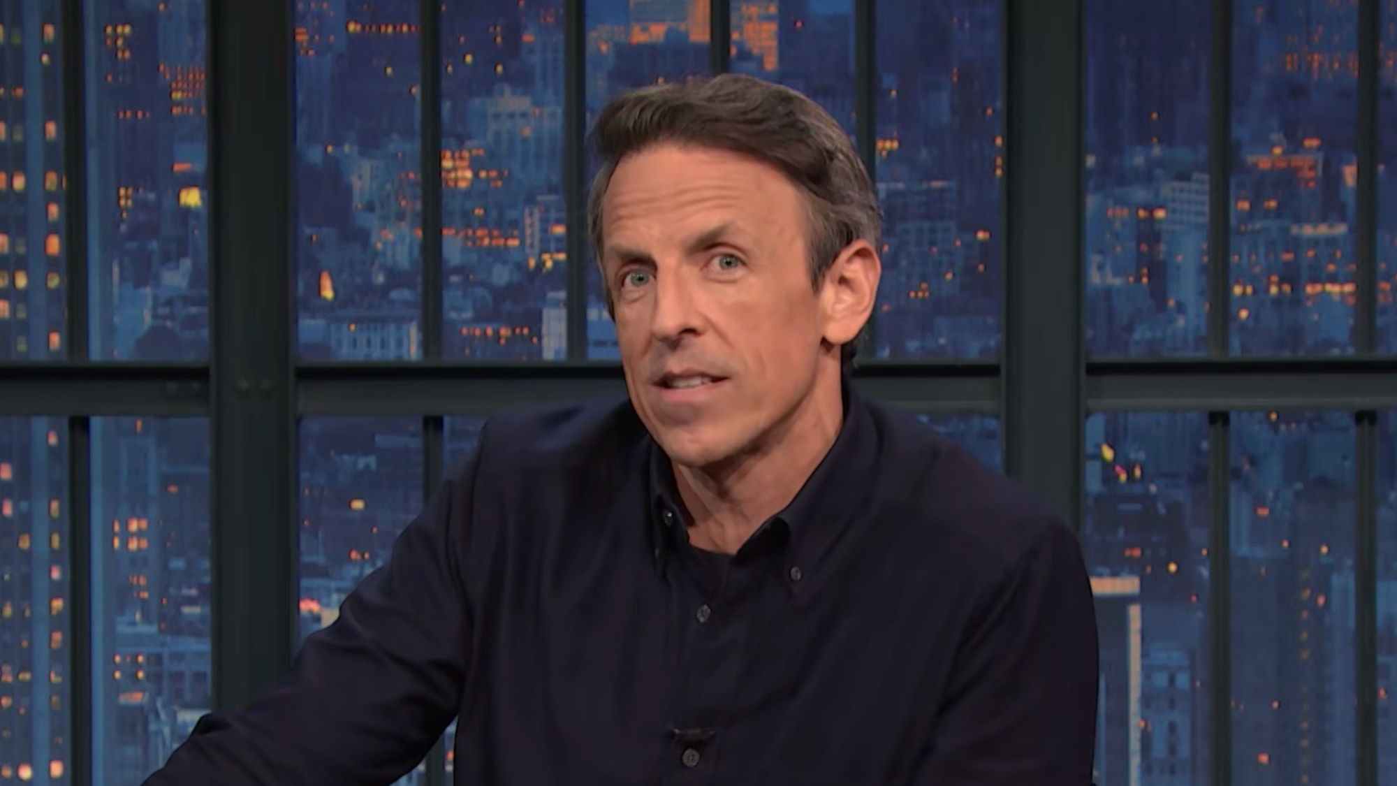 Seth Meyers talks at his desk during a Late Night episode.