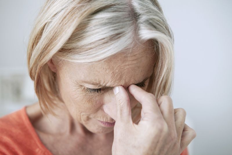 An older woman holds her head in pain.