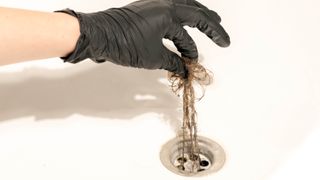 Hair being pulled from a drain with a gloved hand
