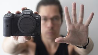 Man holds an empty hand palm first to the camera, with a Canon EOS R5 held in the other hand