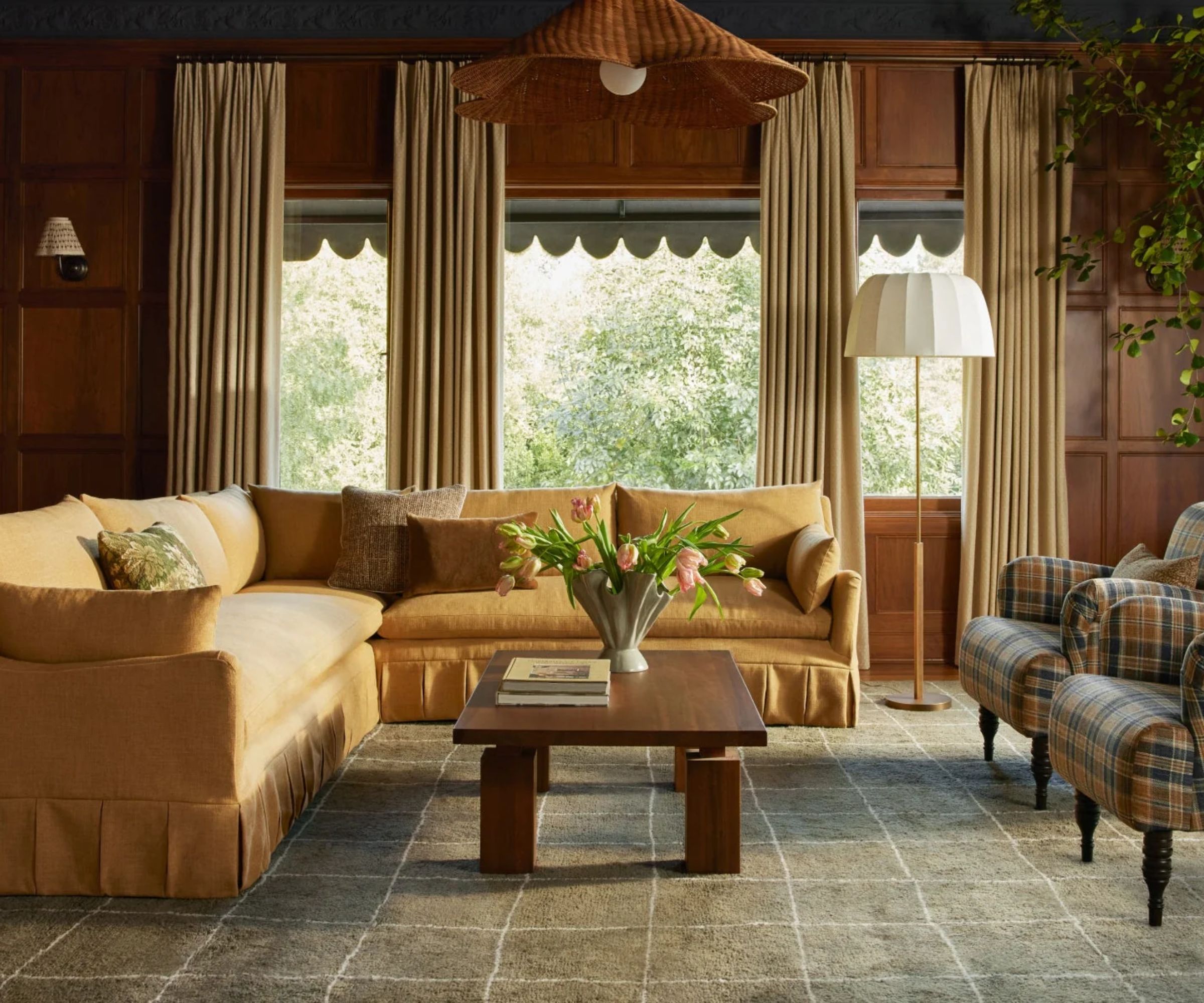 preppy living room with a dark painted ceiling, wooden paneled walls, an earthy green checked rug, deep yellow pleated couch, and two green and ochre plaid arm chairs