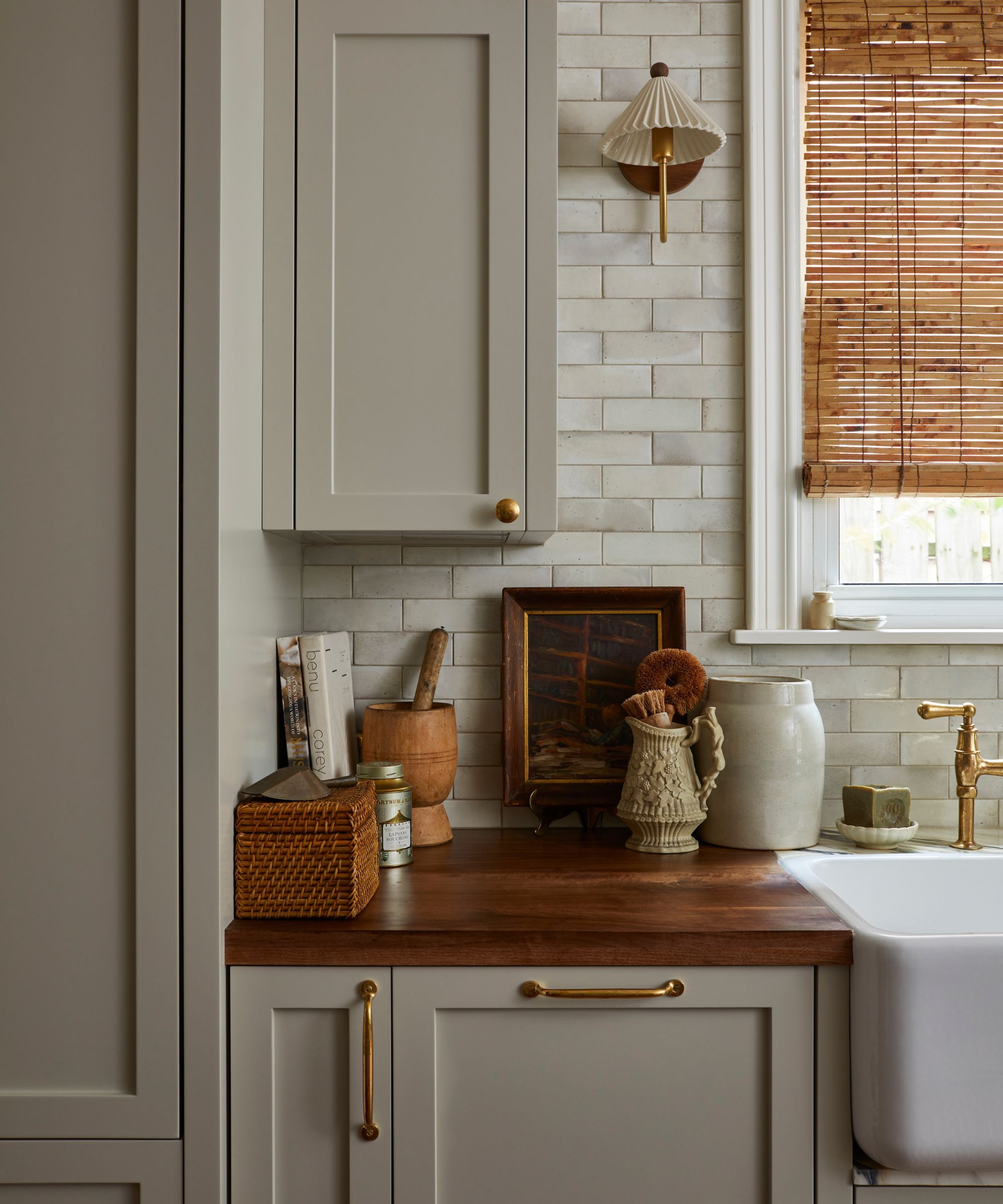 The corner of a galley kitchen with gray cabinetry, wood counters, and collected decor on the countertops