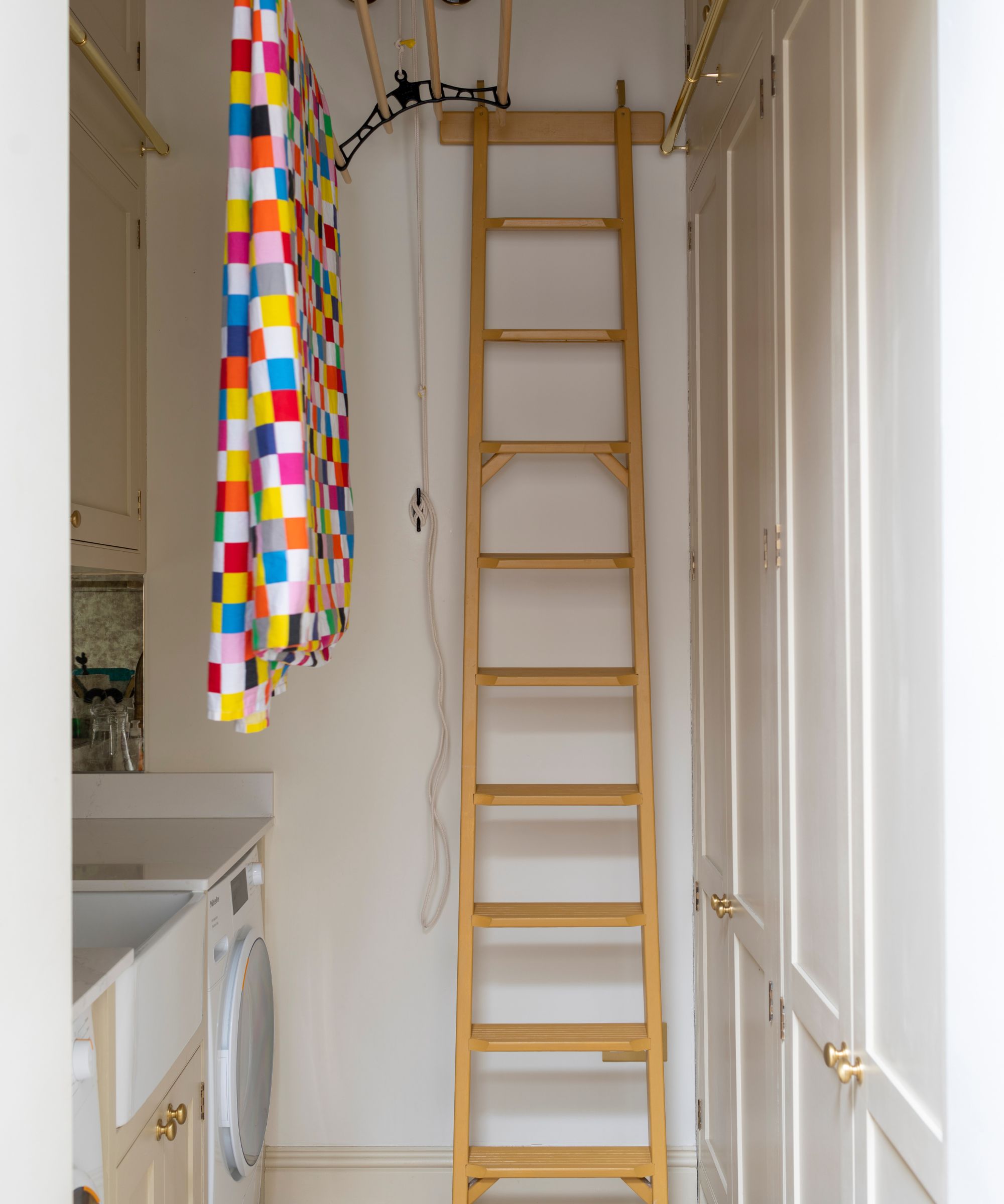 A white utility room with ladder and colorful patterned towel