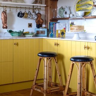 colour ideas for cottagecore decor, yellow kitchen, cottage style with tongue and groove style painted doors, white walls, open shelving, bar stools