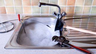 Drain snake, pipe wrench and plunger on stainless steel sink