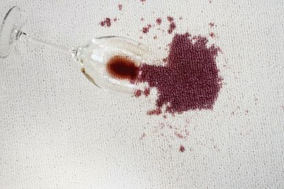 A spilled glass of red wine on a light colored carpet.