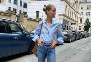 @amaliemoosgaard wearing ablue button-down shirt tucked into straight-leg jeans with black ballet flats and a camel tote bag