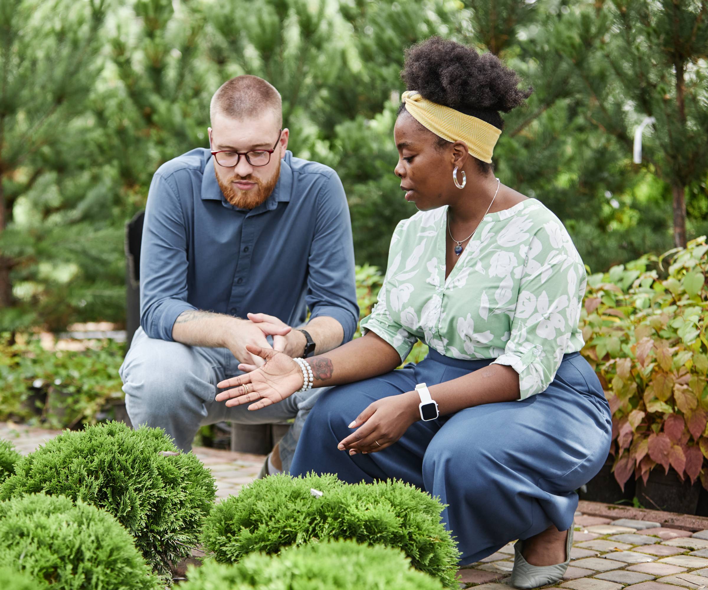 A woman talking to a man while they crouch over shrubs