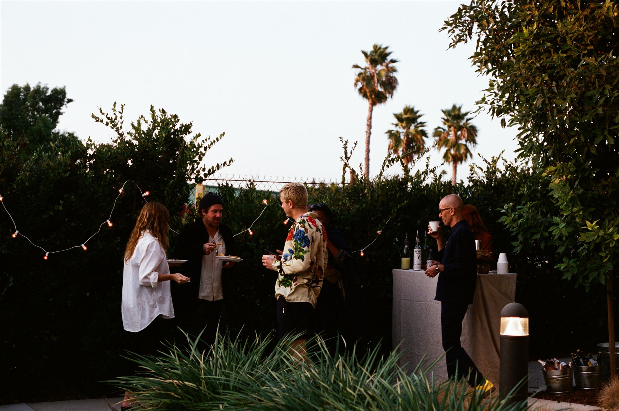 The garden and interior of a design showroom, populated by essentially beautiful furniture or people chatting, immersed in palm trees.