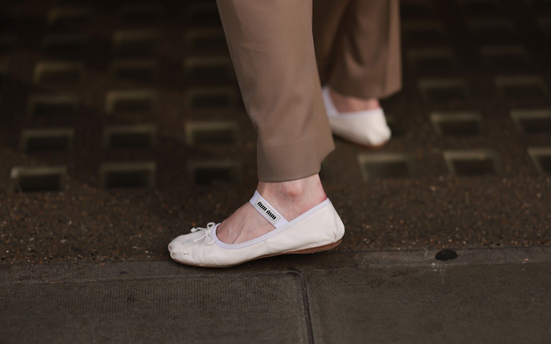 A person shows off cream-colored Miu Miu ballet flats in a street style shot.