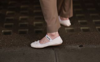 Someone shows off a pair of cream Miu Miu ballet flats in a street style shot.