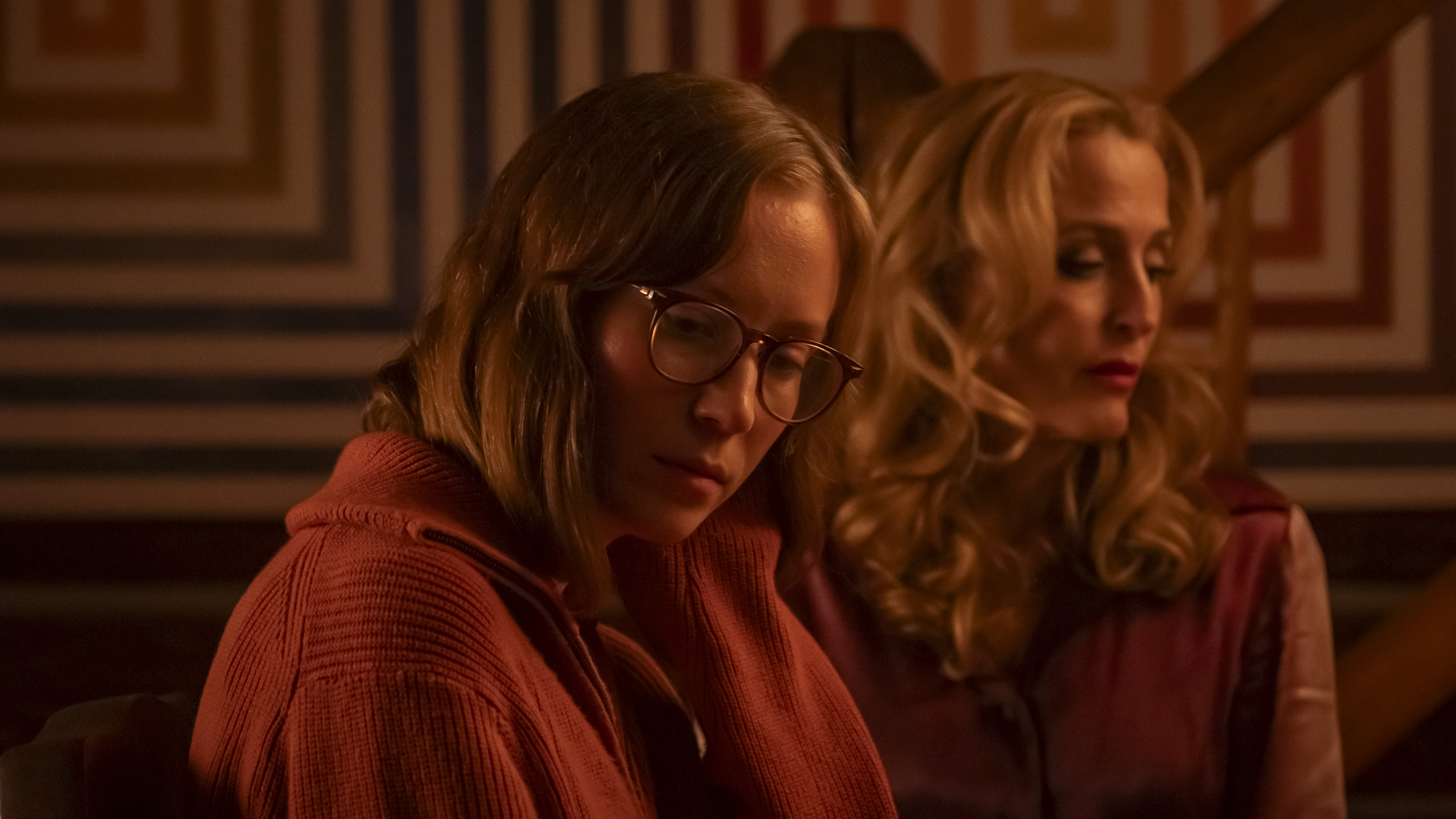 Hannah Einbinder as Kris stands with Gillian Anderson as Billy in front of a wall painted with designs of concentric squares in 'Teenage Sex and Death at Camp Miasma.'