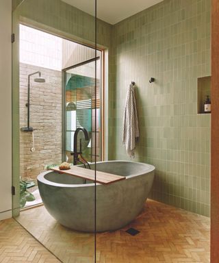 bathroom with freestanding green tub and wooden floor and green tiled walls and outdoor shower