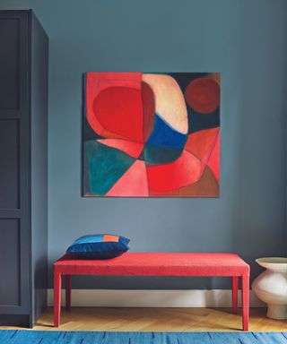 A blue wall with a red bench and a brightly colored painting