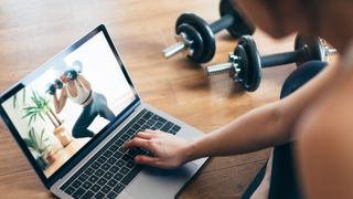 Woman watching a weight workout on a laptop.