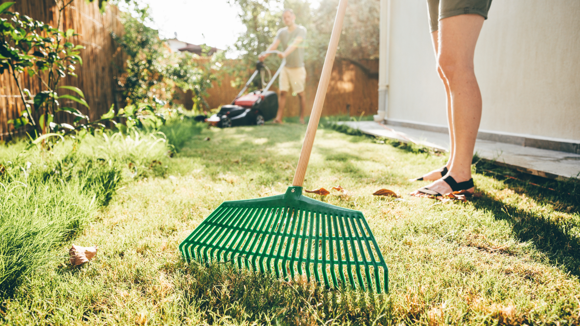 man and woman doing spring lawn care with rake and lawnmower