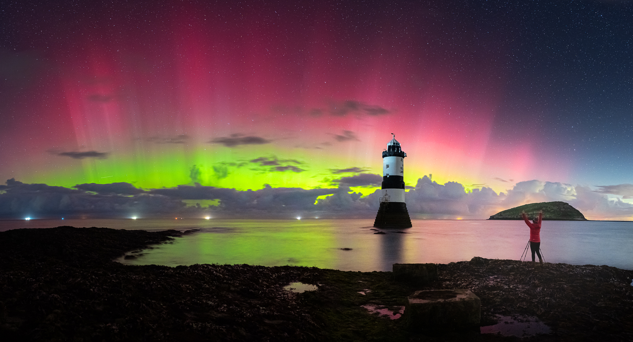 Vibrant green and red shafts of light in the sky above a lighthouse.