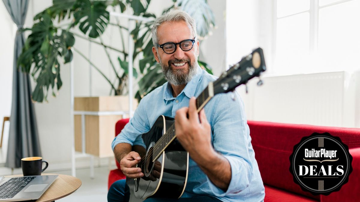 An older man plays acoustic guitar on the sofa