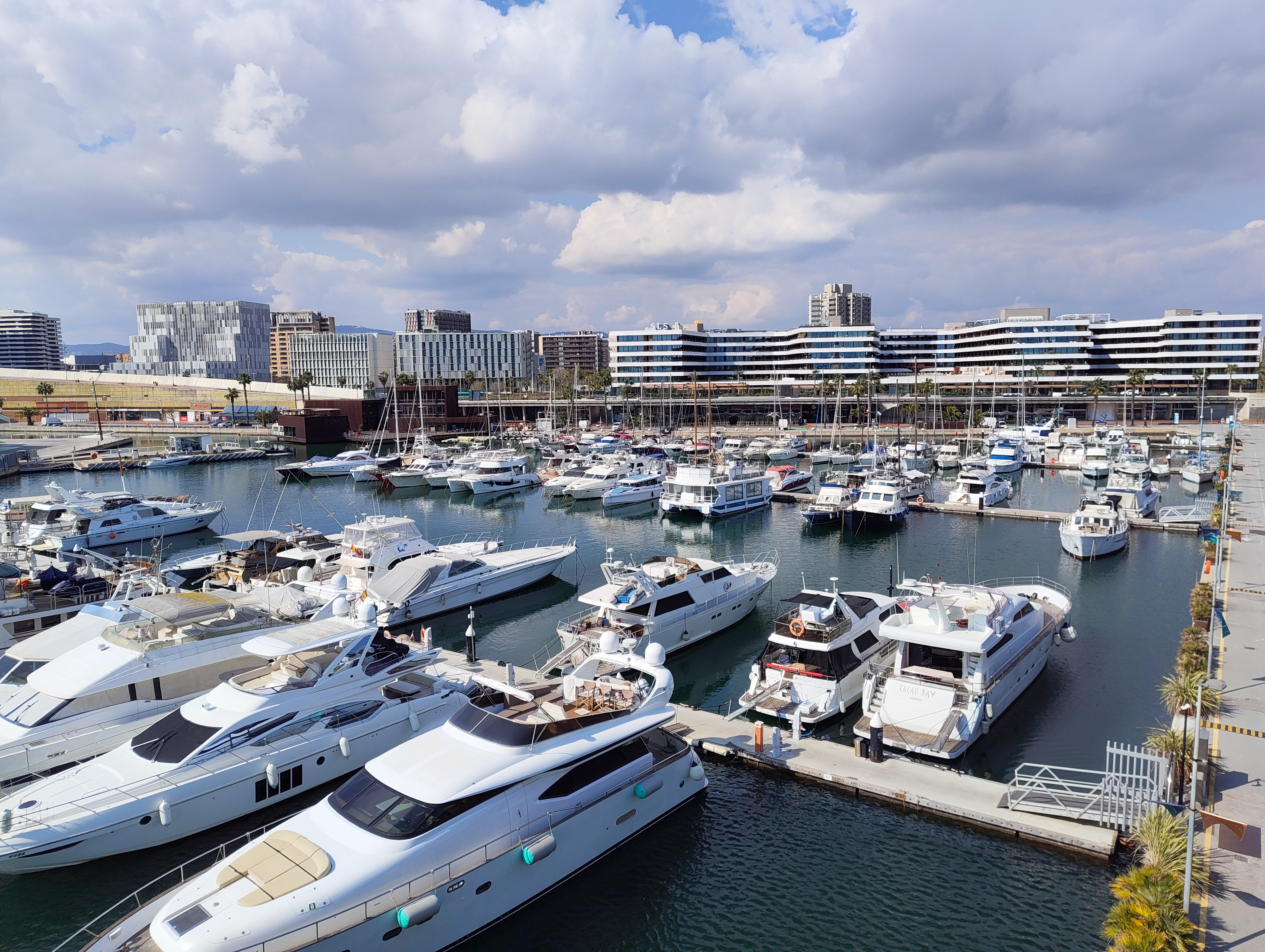 Mid-range view of boats moored in Barcelona&rsquo;s Port Ol&iacute;mpic with modern waterfront buildings in the background, photographed with the Nothing Phone (4a).