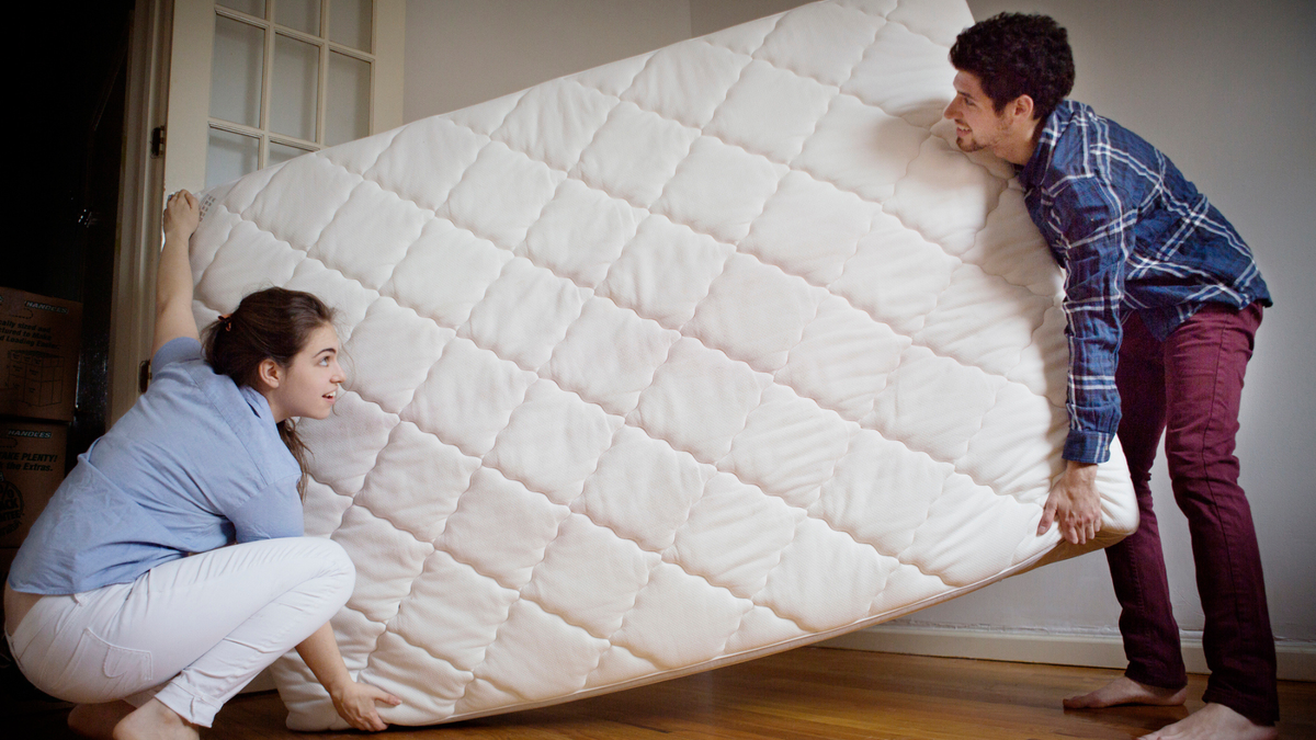 A couple lifting up a mattress to air it out