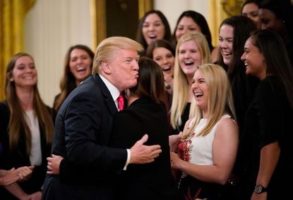  President Donald Trump hugs a member of the Oklahoma women's softball team in the East Room of the White House during an event with NCAA national championship teams on November 17, 2017